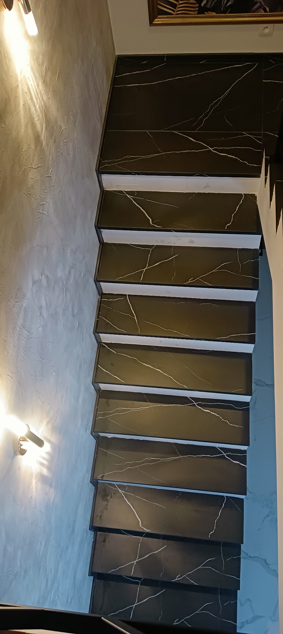 Schody wykończone czarnym marmurem z białymi żyłami, widok z góry na strukturę ściany i oświetlenie.