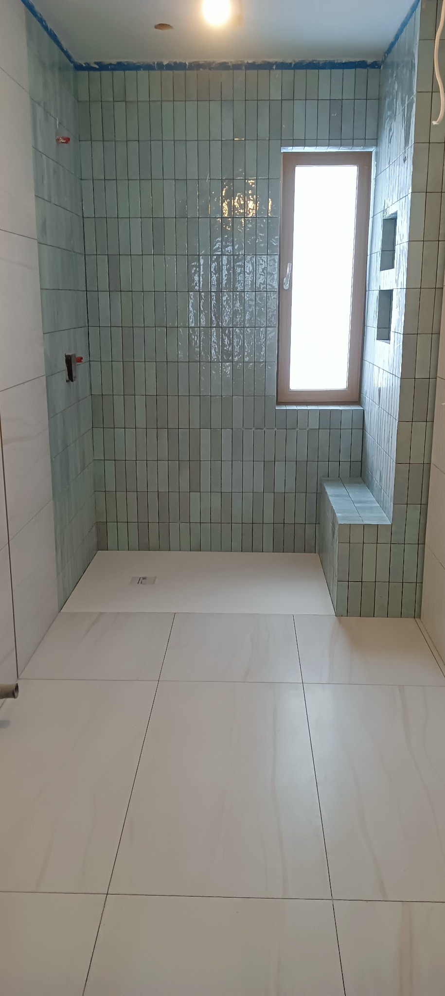 Wykończona łazienka z turkusowymi, pionowo ułożonymi płytkami na ścianach, białymi płytkami podłogowymi i wnęką okienną z siedziskiem.