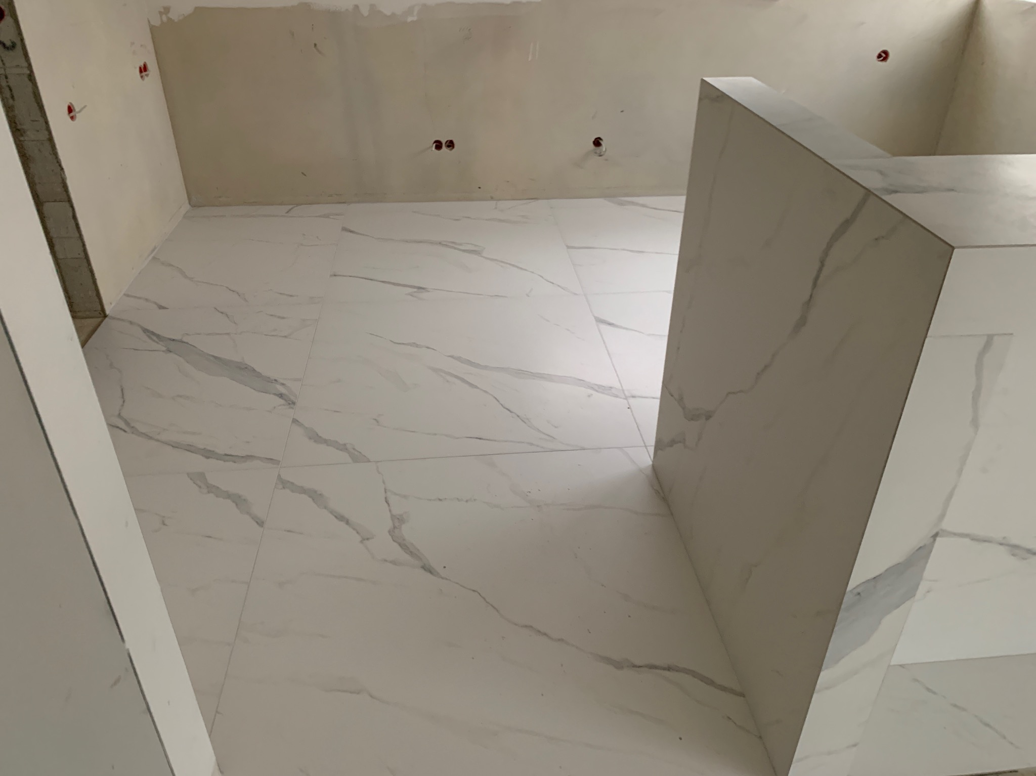 Ułożone białe płytki imitujące marmur na podłodze w trakcie remontu w Raniżowie, widoczne niedokończone ściany i wystające kable.