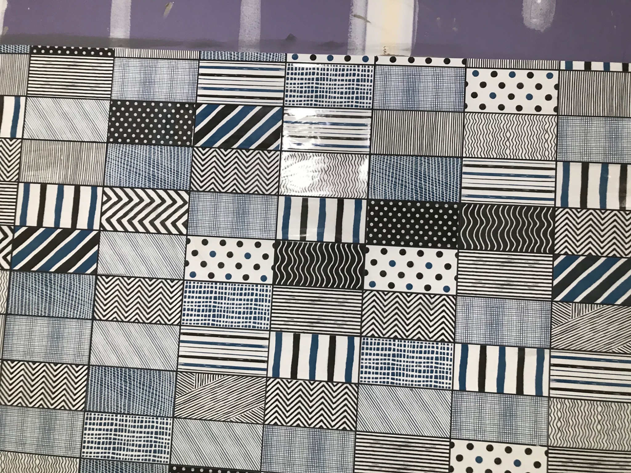 Wzór patchworkowy z płytek w odcieniach bieli, czerni i granatu, zawierający motywy geometryczne: paski, zygzaki, kropki, linie proste i faliste, ułożony na fioletowej ścianie.