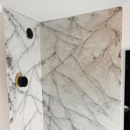 Stylowasciana - Ściana po wykonaniu gładzi z dekoracyjnym motywem gałązek, widoczne otwory instalacyjne z żółtymi elementami, surowy stan wykończenia.