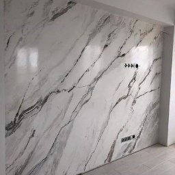 Stylowasciana - Ściana wykończona gładzią imitującą marmur z widocznymi gniazdkami elektrycznymi i fragmentem drewnianej podłogi.