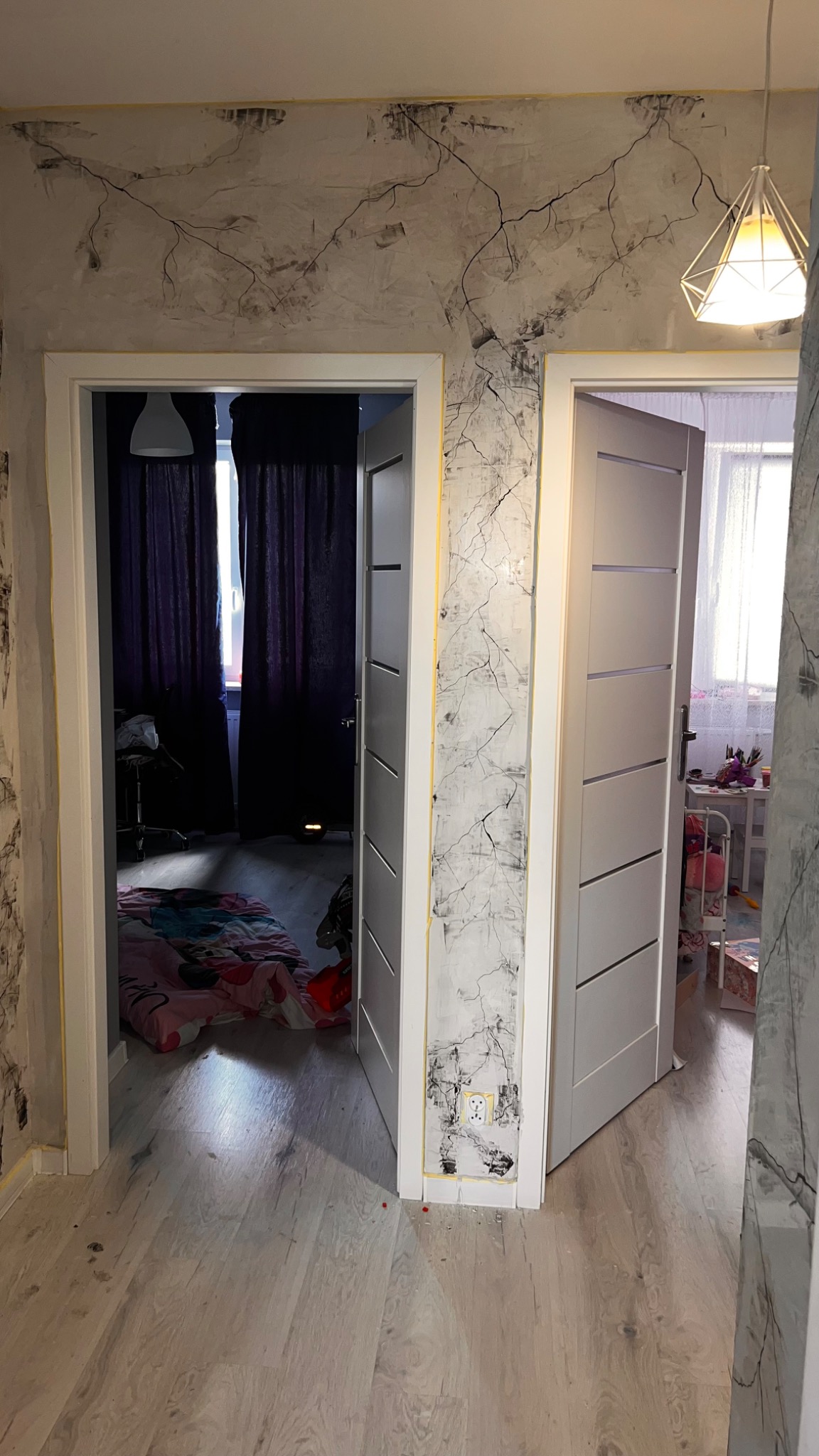 Korytarz po remoncie z dwoma białymi drzwiami, ściany wykończone dekoracyjną strukturą imitującą pęknięcia, widoczne niedociągnięcia przy gniazdku i żółta taśma malarska pod sufitem.