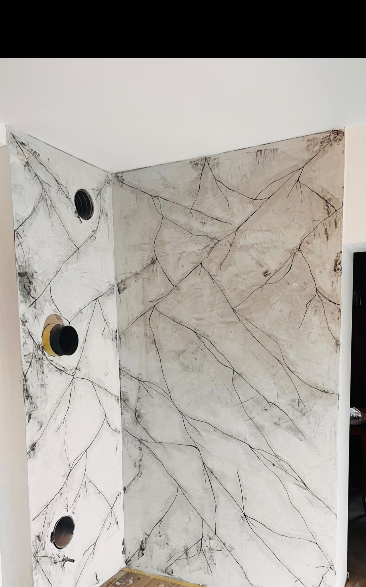 Ściana po wykonaniu gładzi z dekoracyjnym motywem gałązek, widoczne otwory instalacyjne z żółtymi elementami, surowy stan wykończenia.