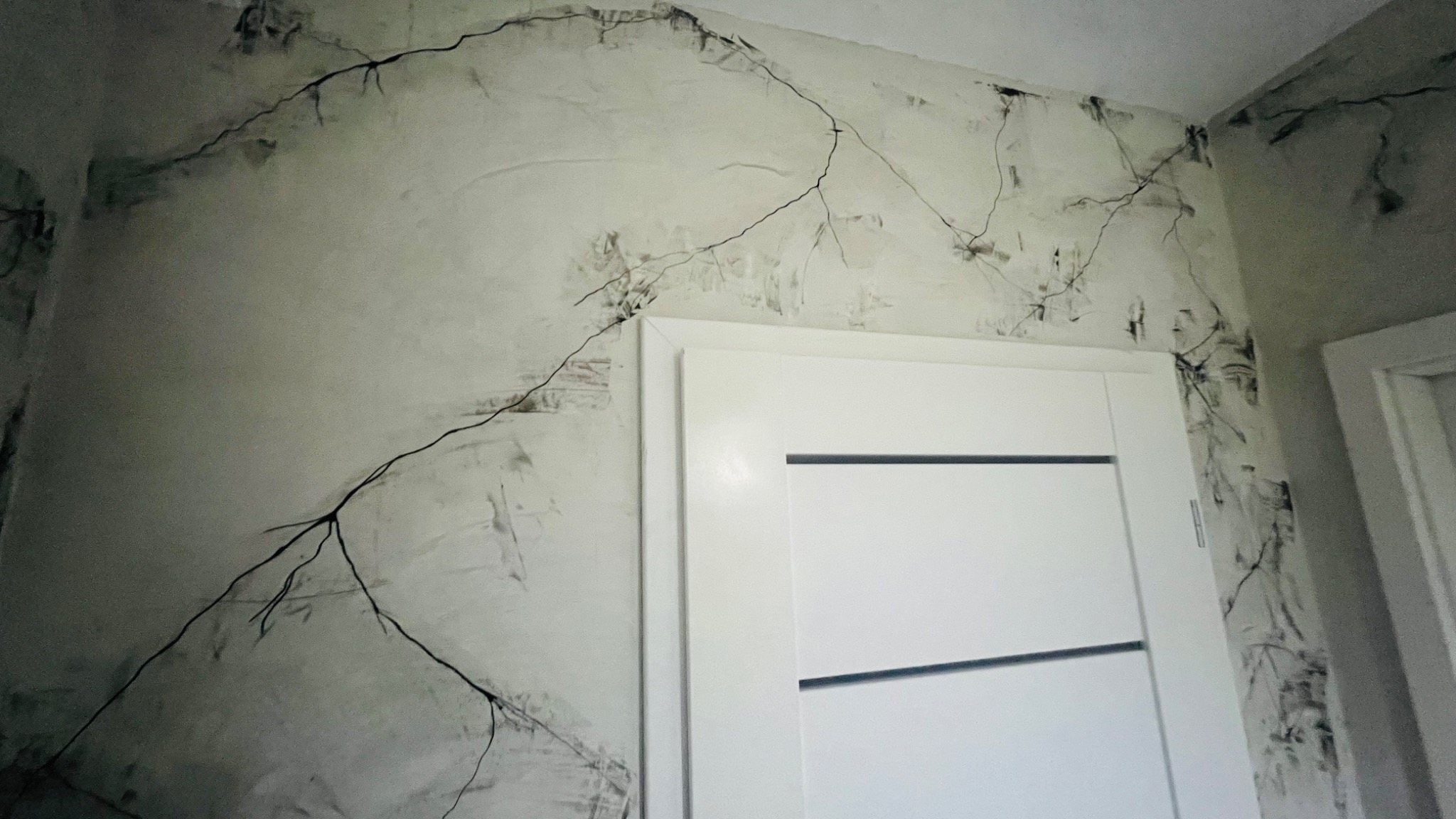 Ściana z dekoracyjną fakturą imitującą pęknięcia, w tle białe drzwi wewnętrzne z poziomymi frezami.