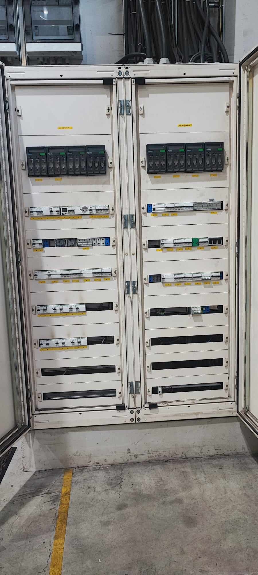 Otwarta szafa elektryczna z widocznymi zabezpieczeniami, wyłącznikami i przewodami wewnątrz.