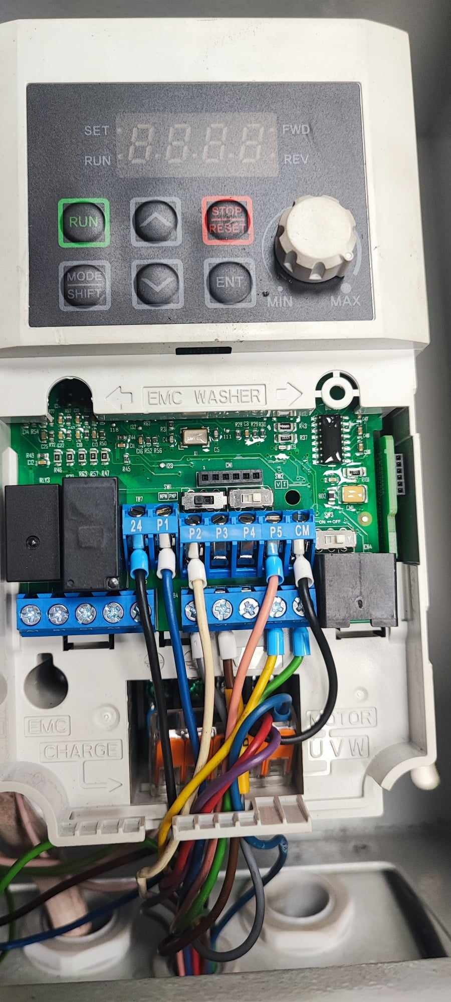 Otwarta obudowa falownika z widocznymi podłączonymi przewodami o różnych kolorach do listwy zaciskowej, wyświetlacz cyfrowy w górnej części obudowy.