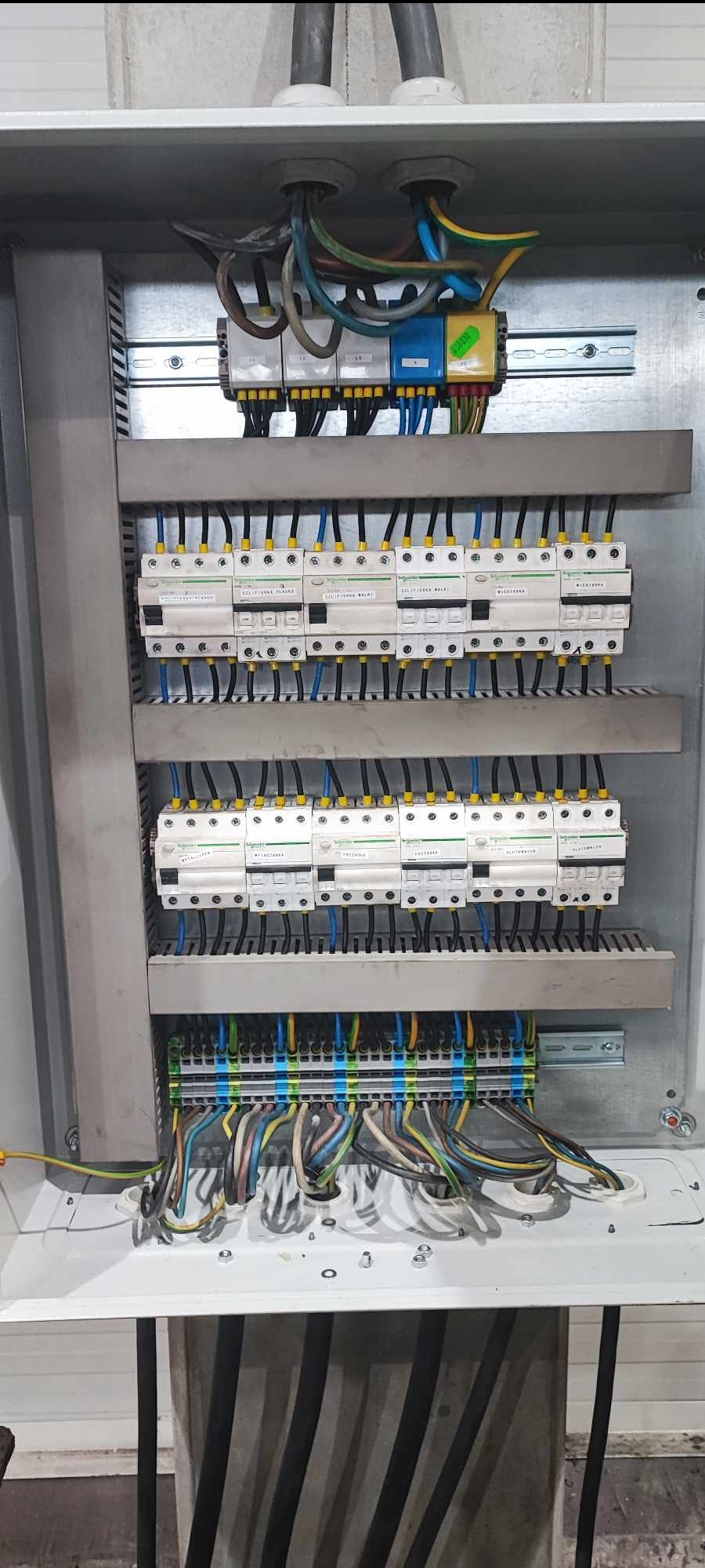 Rozdzielnica elektryczna z widocznymi bezpiecznikami, przewodami i listwami zaciskowymi, zasilanie doprowadzone przewodami w peszlach.