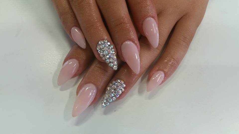 Dłonie z migdałowymi paznokciami w kolorze pudrowego różu, dwa z nich ozdobione drobnymi, błyszczącymi kryształkami ułożonymi w kształt łezki.