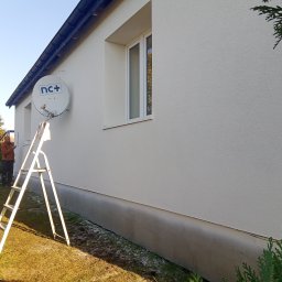 F.U. Mirax Mirosław Grzesiak - Świeżo pomalowana elewacja domu jednorodzinnego w jasnym odcieniu, z widoczną białą anteną satelitarną NC+, drabina oparta o ścianę i pracownik w pomarańczowej kurtce przy oknie.