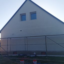 F.U. Mirax Mirosław Grzesiak - Dom jednorodzinny z szarą elewacją, częściowo zasłonięty przez metalowe rusztowanie, z widocznymi wiadrami z farbą u dołu, sugerującymi prace wykończeniowe.