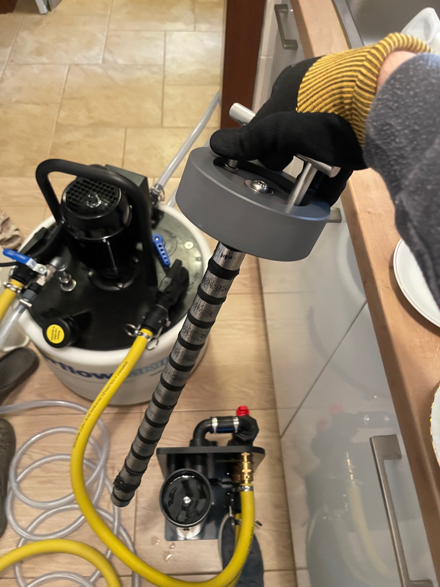 Czyszczenie instalacji centralnego ogrzewania przy użyciu specjalistycznego urządzenia z żółtymi wężami, widoczne elementy armatury i rękawica ochronna.