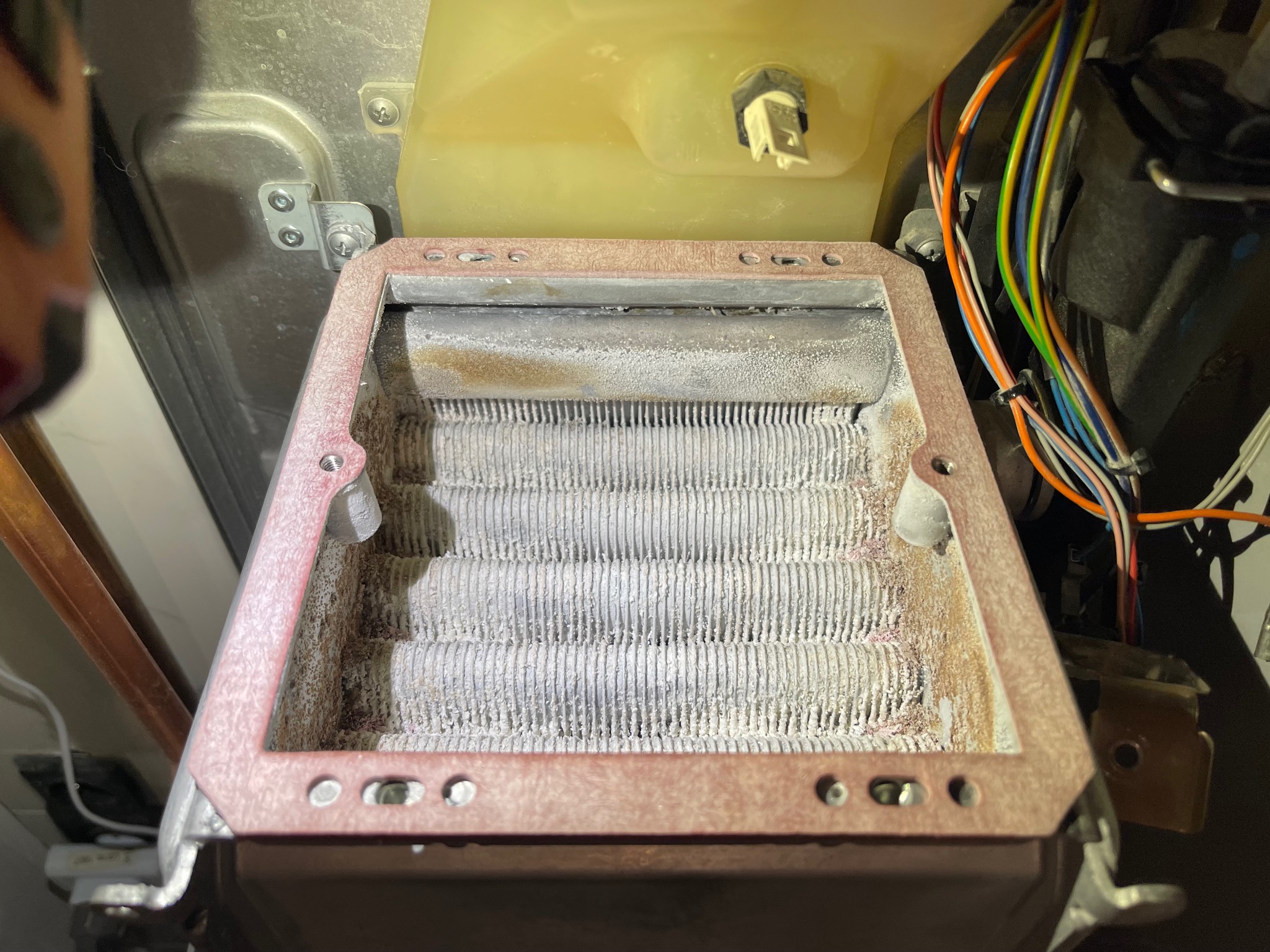 Zdemontowany, silnie zakurzony wymiennik ciepła z kotła gazowego, widoczne przewody elektryczne i elementy obudowy.