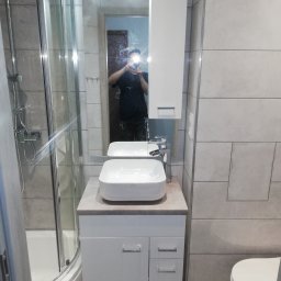 Remonty wykończenia mieszkań domów - Wykończona łazienka z kabiną prysznicową, umywalką nablatową na szafce z szufladami, lustrem z szafką i ukrytą klapą rewizyjną w płytkach.