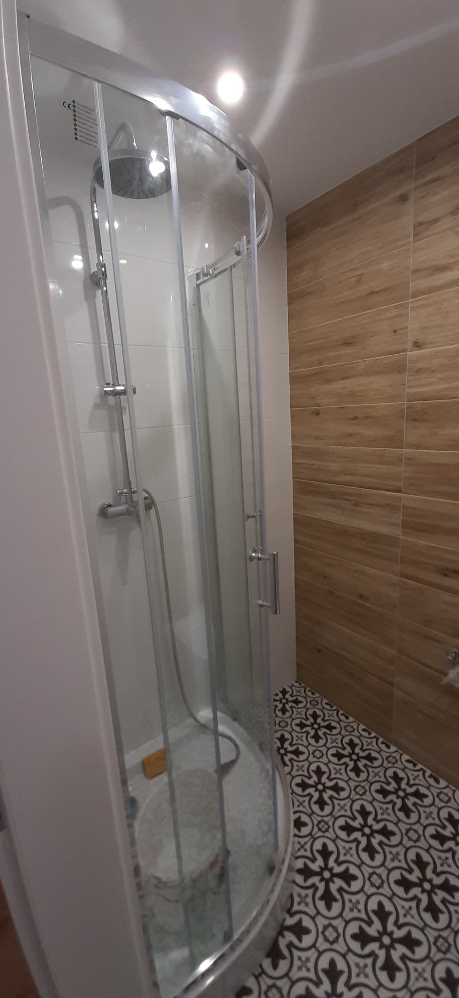 Nowoczesna kabina prysznicowa z chromowanymi elementami i szkłem, w łazience z drewnopodobnymi płytkami ściennymi i wzorzystą podłogą.