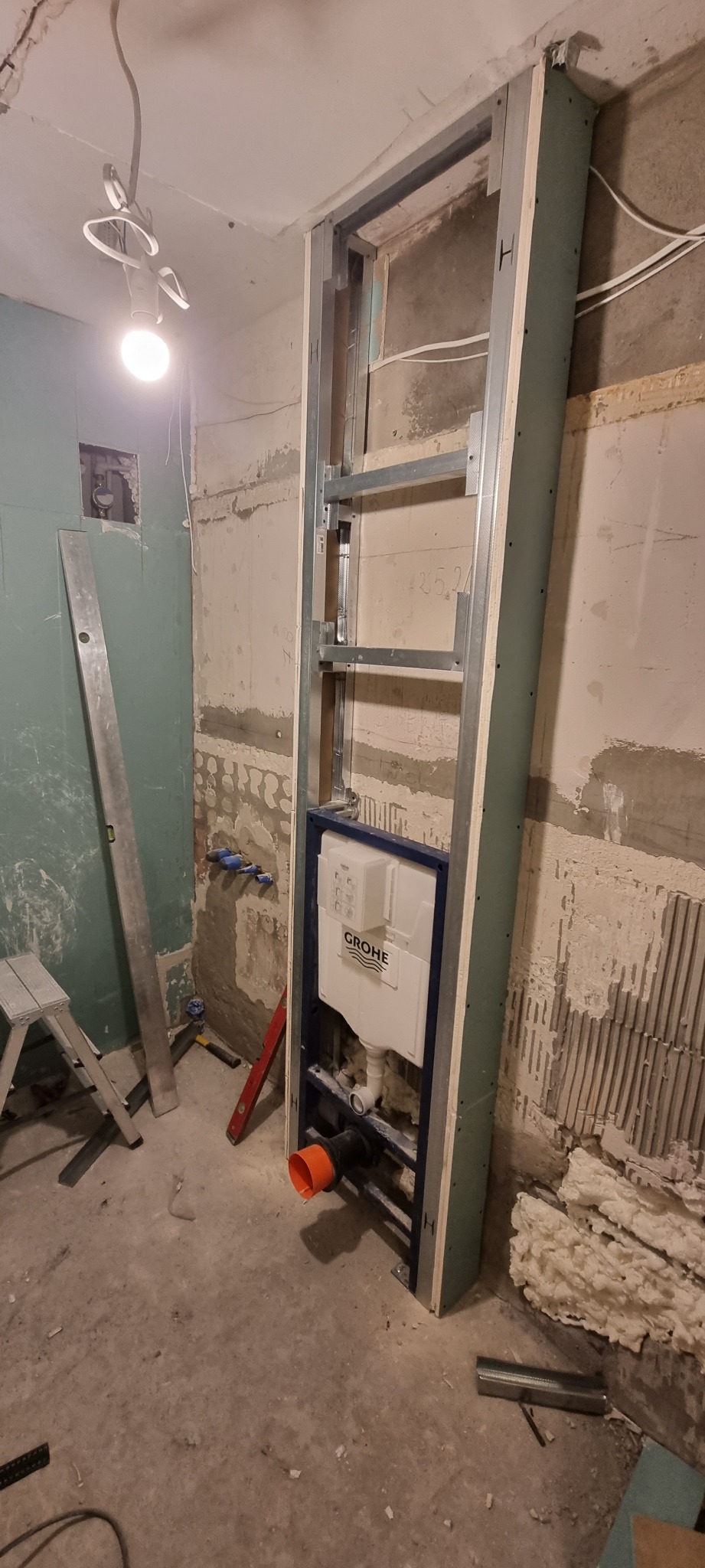 Stelaż podtynkowy z zamontowaną spłuczką Grohe w trakcie prac w łazience w Łodzi, widoczne profile, płyta karton gips, poziomica i fragment ściany z resztkami starej glazury.