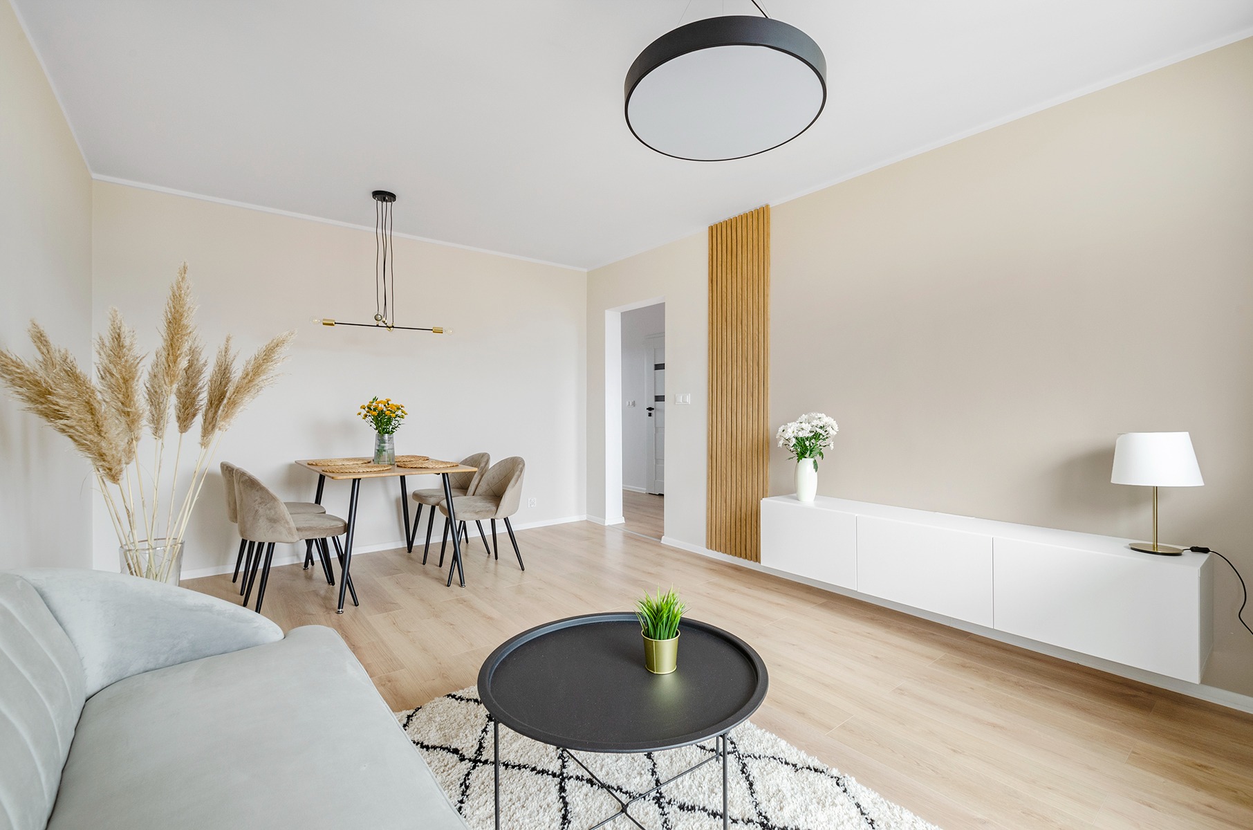 Jasne wnętrze salonu z drewnianą ścianką dekoracyjną, stołem z kwiatami i minimalistycznym oświetleniem.