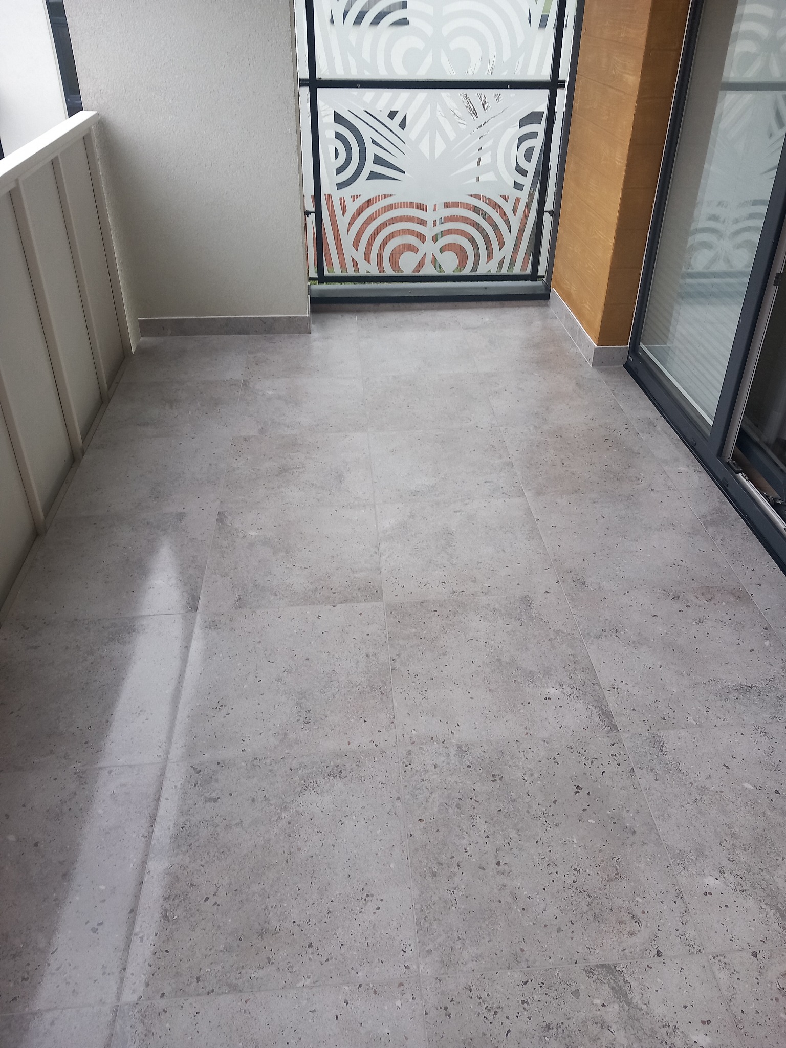 Szare płytki podłogowe na balkonie z dekoracyjną szybą balkonową z motywem roślinnym i przesuwnymi drzwiami balkonowymi