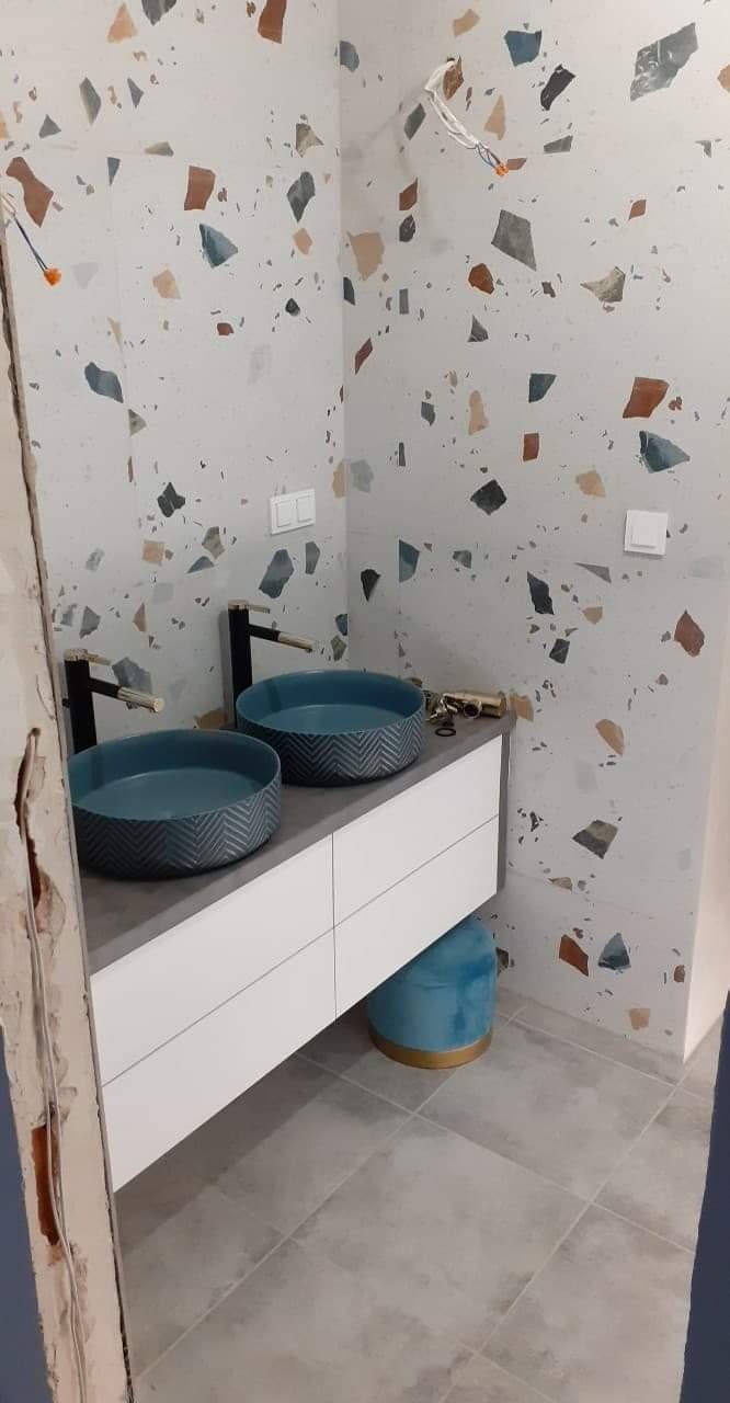 Nowoczesna łazienka z dwoma okrągłymi, niebieskimi umywalkami z wzorem w jodełkę, bateria w kolorze szczotkowanego złota, biała szafka pod umywalką i ściany wykończone płytkami w stylu lastryko.