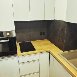 PSP PIOTR GOLEC GITCHATA - Nowoczesna kuchnia z białymi szafkami, drewnianym blatem, płytą indukcyjną i stalowym piekarnikiem. Ciemna ściana nad blatem z gniazdkami elektrycznymi.