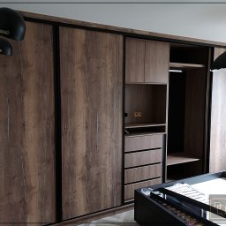 Dobre Quchnie S.C - Szafa wnękowa z przesuwnymi drzwiami w odcieniach brązu i czerni, z widocznymi półkami i szufladami, oświetlona lampą wiszącą i kinkietem, z logo firmy w prawym dolnym rogu.