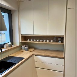 Dobre Quchnie S.C - Jasna kuchnia na wymiar w Cieszynie z drewnianym blatem, czarnym zlewem i rzędem filiżanek na półce, uzupełniona o ekspres do kawy.