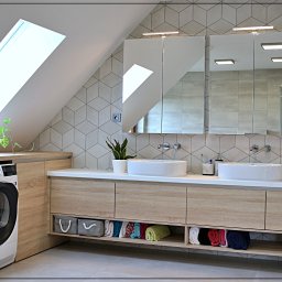 Dobre Quchnie S.C - Jasna łazienka na poddaszu w Cieszynie z drewnianą szafką pod umywalką, pralką i suszarką Electrolux oraz geometrycznymi płytkami na ścianie.