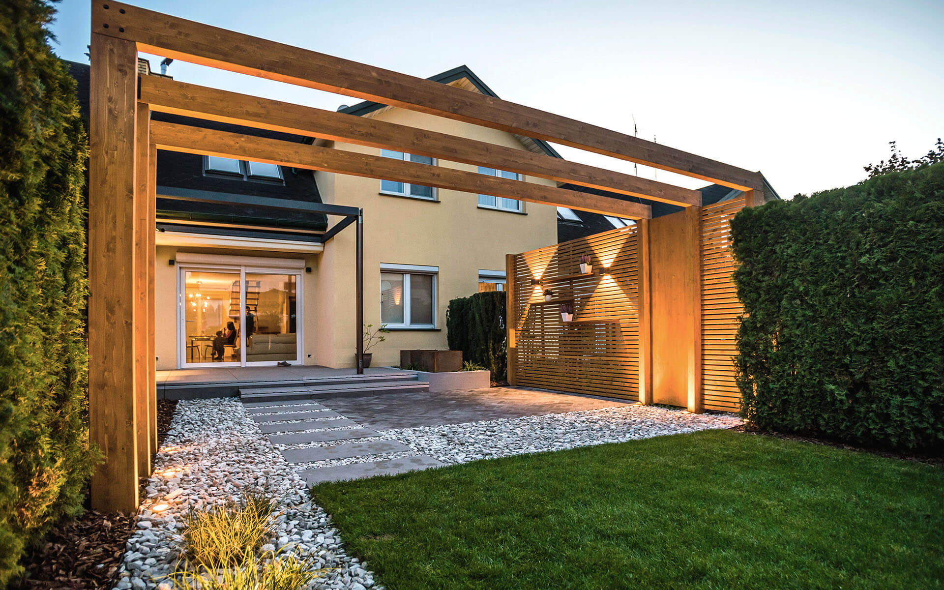 Nowoczesna drewniana konstrukcja z oświetleniem punktowym w ogrodzie, z elementami dekoracyjnymi i ścieżką z kamieni.