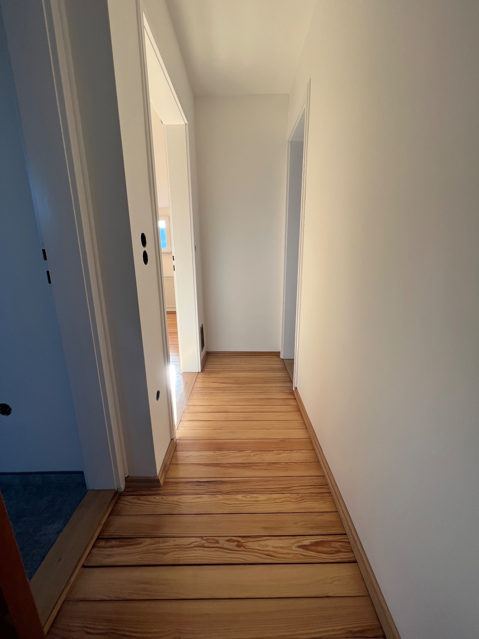 Korytarz po remoncie: świeżo pomalowane białe ściany i ułożona drewniana podłoga z widocznymi słojami.