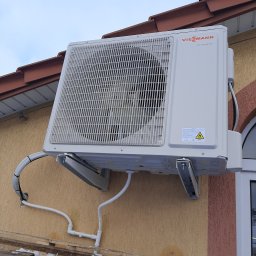 ARKOS - INSTAL ARKADIUSZ STENKA - Zewnętrzna jednostka klimatyzacji Viessmann DC Inverter zamontowana na elewacji budynku, widoczne rury instalacyjne i fragment dachu z dachówką.