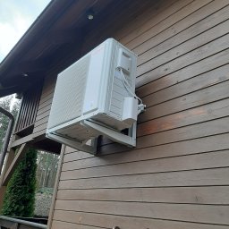 ARKOS - INSTAL ARKADIUSZ STENKA - Biała pompa ciepła marki Viessmann zamontowana na brązowej drewnianej elewacji domu, widoczna drabina oparta o ścianę.