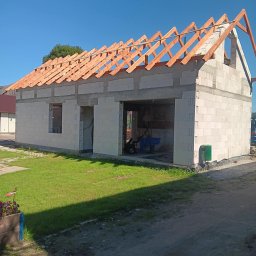 Viking_Dom Adrian Wiczling - Budowa domu jednorodzinnego w stanie surowym otwartym. Widoczne ściany z bloczków i drewniana konstrukcja dachu na tle błękitnego nieba.