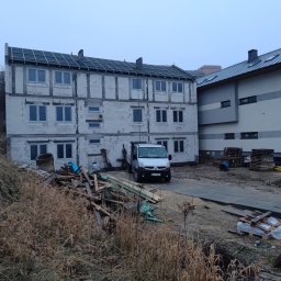 Viking_Dom Adrian Wiczling - Trzy kondygnacyjny budynek w stanie surowym otwartym z częściowo wykonanym dachem, na pierwszym planie sterta drewna, samochód dostawczy i otoczenie placu budowy.