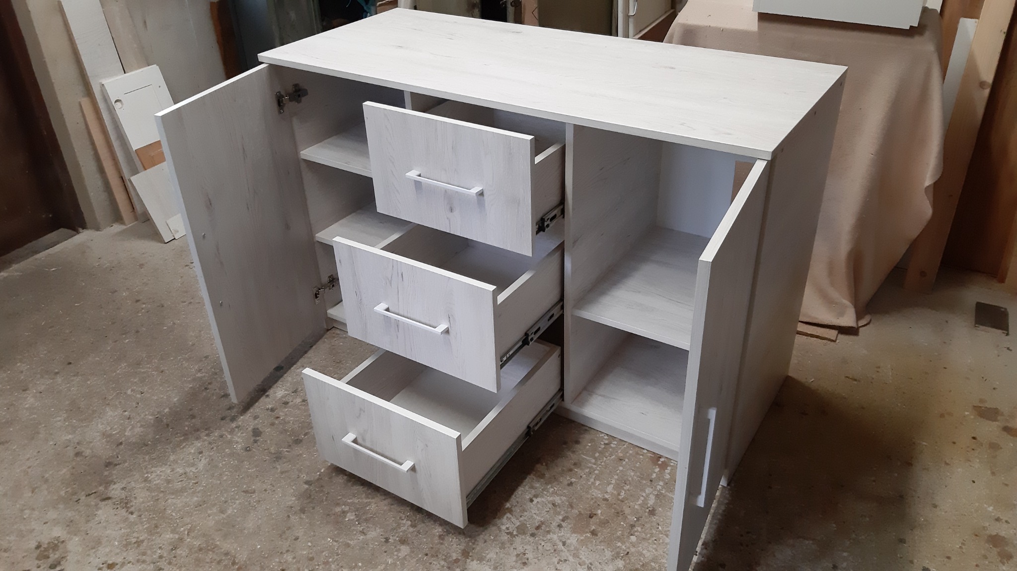 Komoda z szufladami i półkami z jasnego drewna, wykonana w Kętach, z otwartymi drzwiczkami, prezentująca wnętrze i mechanizmy szuflad.