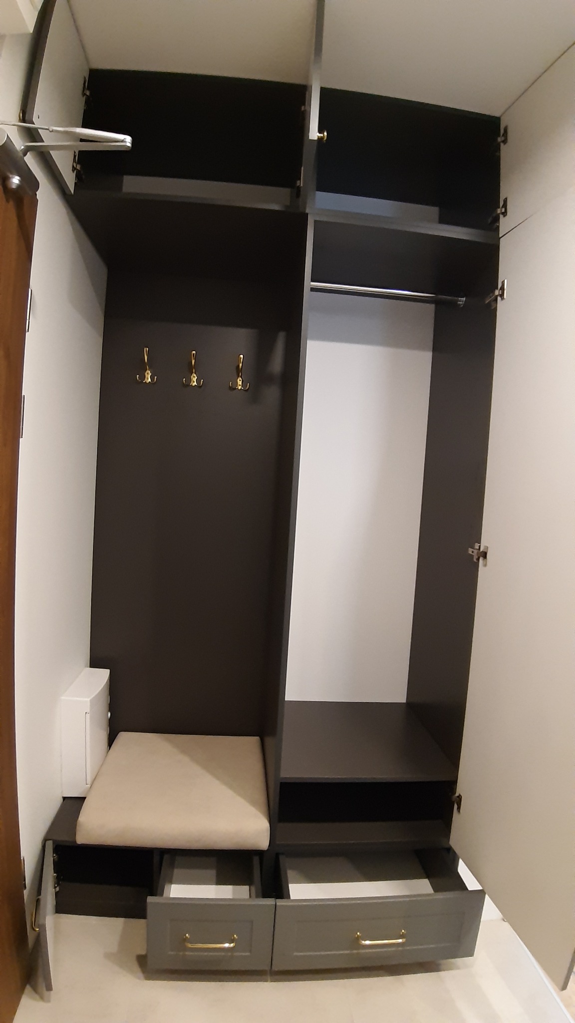 Wnętrze szafy wnękowej z siedziskiem i wysuwanymi szufladami w odcieniach szarości, widoczne złote haczyki na ubrania i drążek na wieszaki.