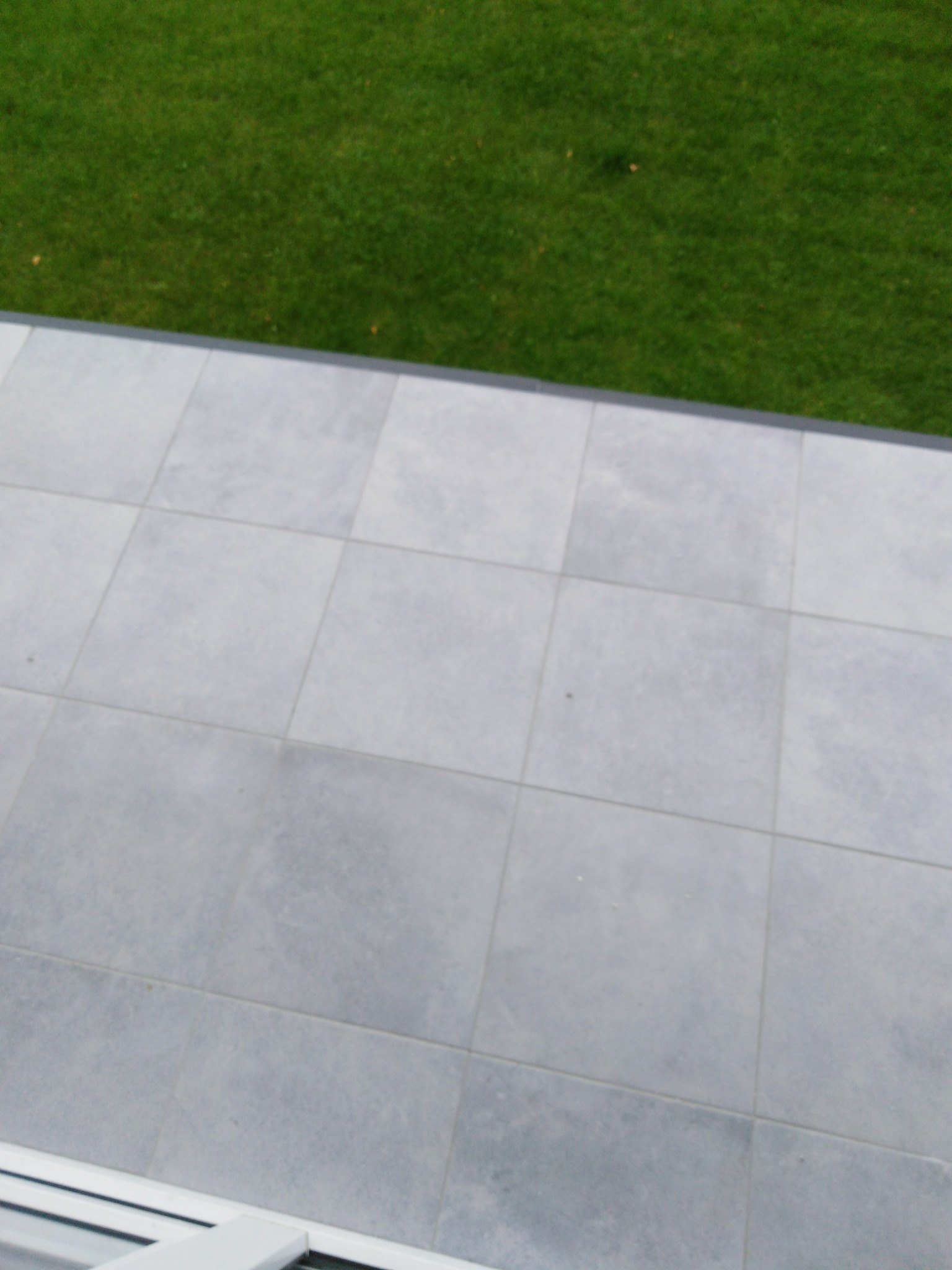 Szare płytki na balkonie z widocznym fragmentem trawnika za barierką.