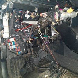 AUTO SERWIS KUBIAK PIOTR KUBIAK - Wnętrze samochodu z rozebraną deską rozdzielczą, widoczne liczne przewody, bezpieczniki i elementy mechaniczne układu kierowniczego.