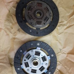 AUTO SERWIS KUBIAK PIOTR KUBIAK - Dwie tarcze sprzęgłowe, używana i nowa, leżące na brązowym papierze. Górna tarcza jest zużyta, dolna nowa z widocznym logo Valeo.