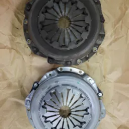 Używane sprzęgło samochodowe obok nowego sprzęgła marki Valeo na brązowym papierze pakowym.