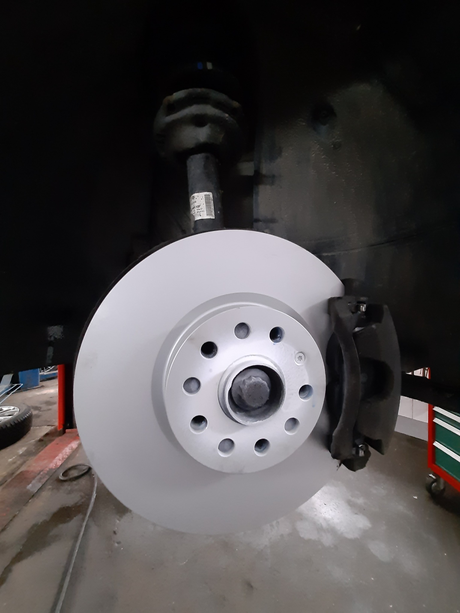 Nowa tarcza hamulcowa zamontowana w samochodzie, widoczny zacisk hamulcowy i element zawieszenia w warsztacie.