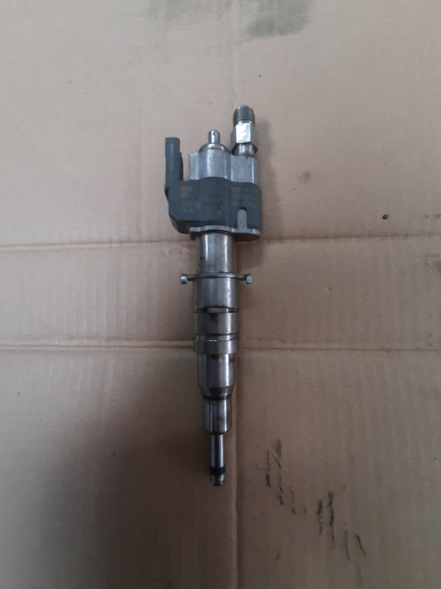 Pojedynczy, używany wtryskiwacz paliwa Common Rail, leżący na kartonowym podłożu.