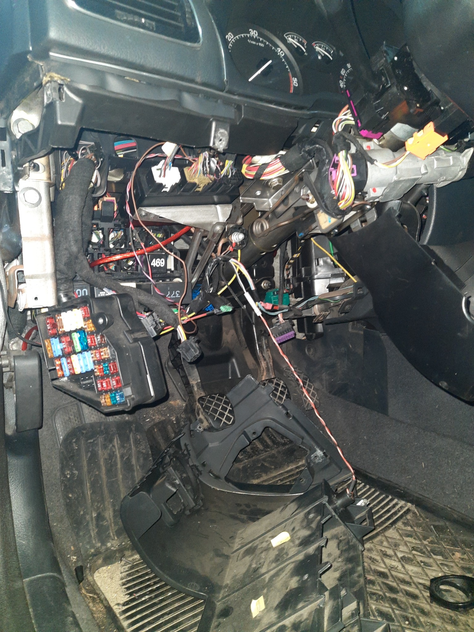 Wnętrze samochodu z rozebraną deską rozdzielczą, widoczne liczne przewody, bezpieczniki i elementy mechaniczne układu kierowniczego.