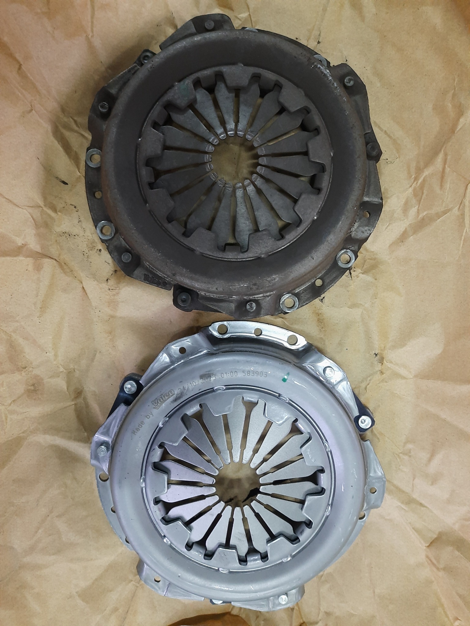 Używane sprzęgło samochodowe obok nowego sprzęgła marki Valeo na brązowym papierze pakowym.