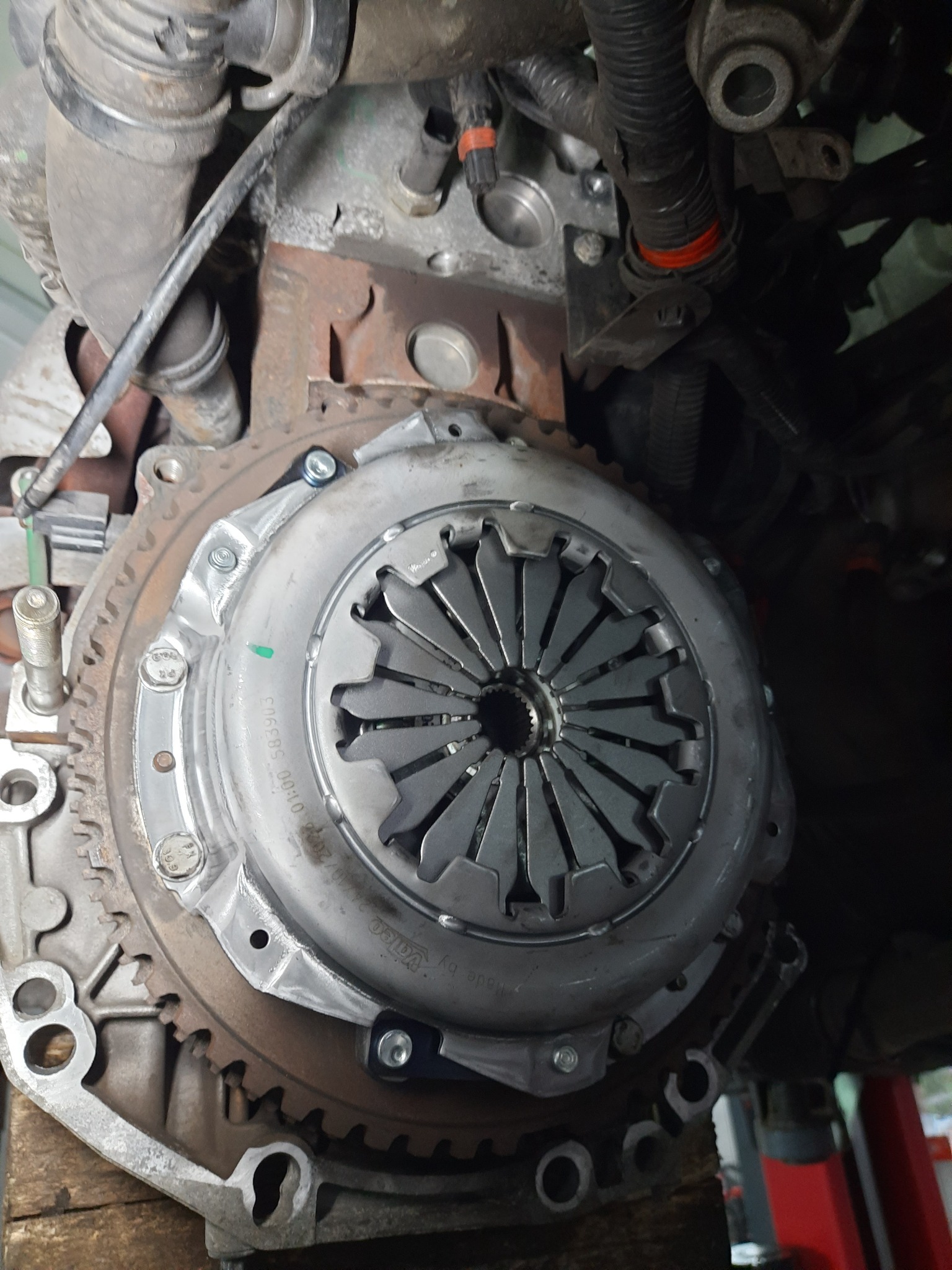 Widok sprzęgła samochodowego z widocznymi tarczami i elementami mocującymi, zamontowanego w pojeździe, z widocznymi przewodami i elementami silnika w tle.