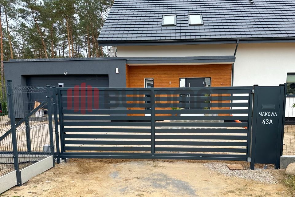 Nowoczesna, pozioma brama wjazdowa w kolorze grafitowym z numerem domu 'Makowa 43A', na tle domu z elementami drewna i szarego tynku, obok fragment siatki ogrodzeniowej.