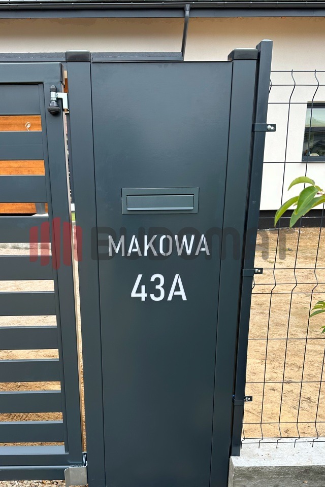 Nowoczesna, grafitowa brama wjazdowa z skrzynką na listy i numerem domu 'Makowa 43A', przylegająca do metalowej siatki ogrodzeniowej i fragmentu ogrodzenia panelowego.