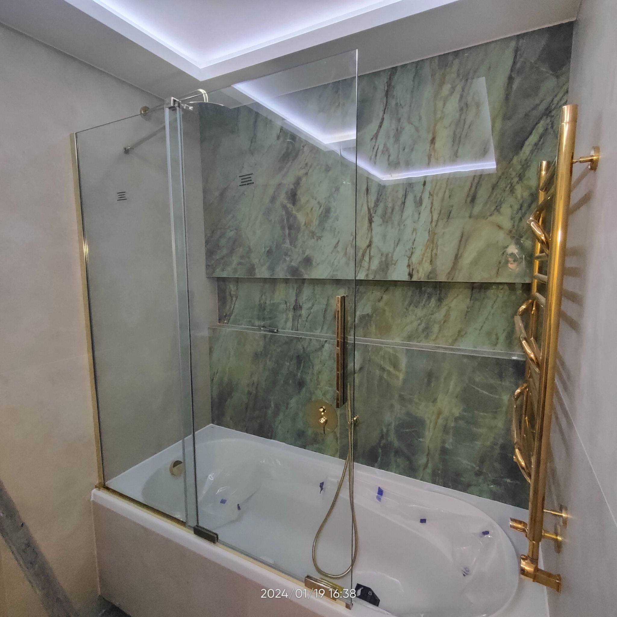 Nowoczesna łazienka z wanną jacuzzi, szklanym parawanem nawannowym z elementami w kolorze złotym oraz marmurową ścianą z podświetleniem LED.