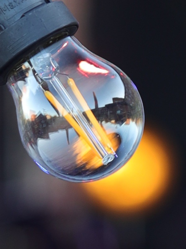 Żarówka LED z widocznym odbiciem budynków w szkle, oświetlona ciepłym, rozmytym światłem w tle.