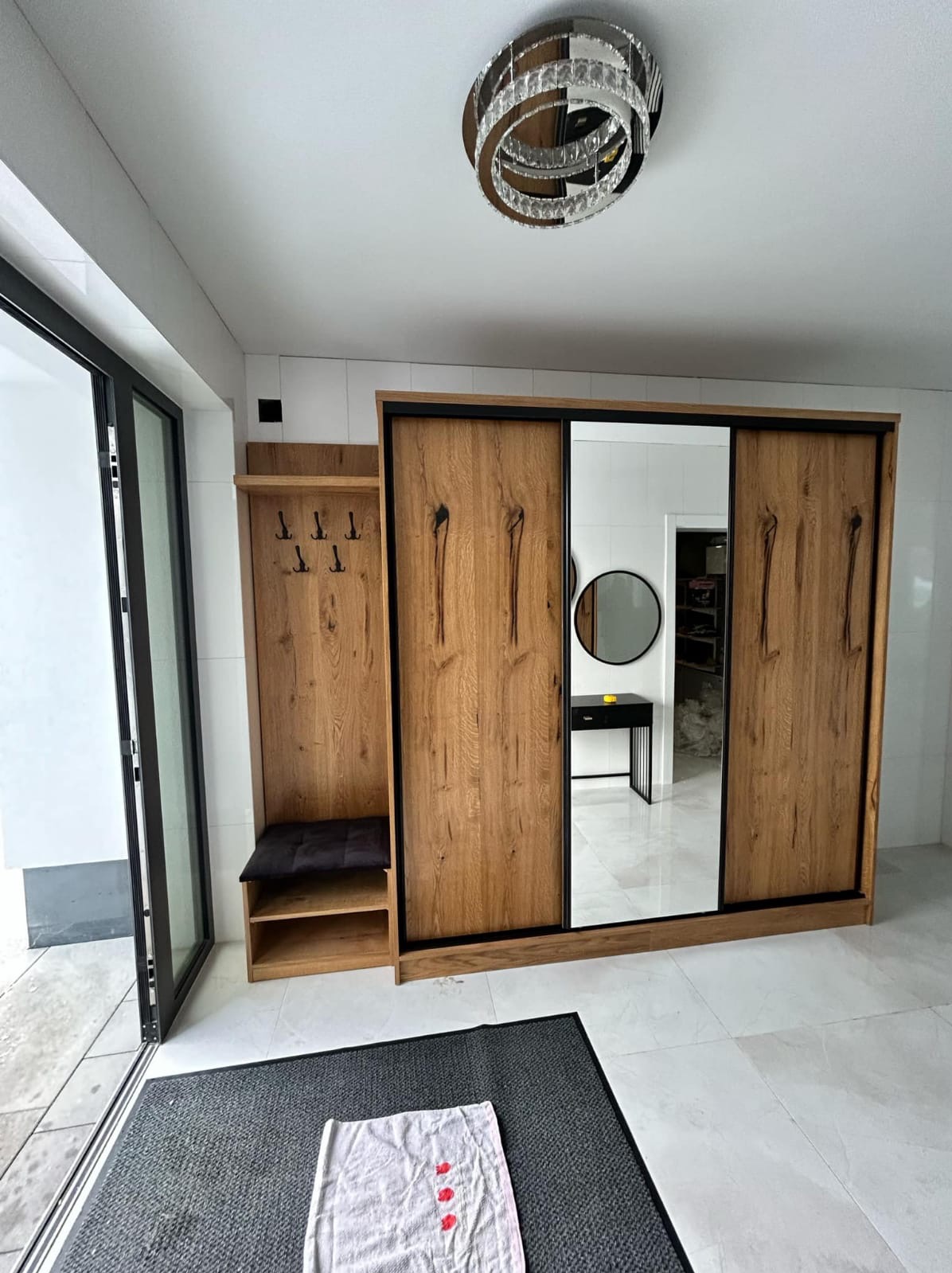 Drewniana szafa przesuwna z lustrem i wieszakiem w przedpokoju w Kalwarii Zebrzydowskiej. Widoczny dywanik i nowoczesna lampa sufitowa.