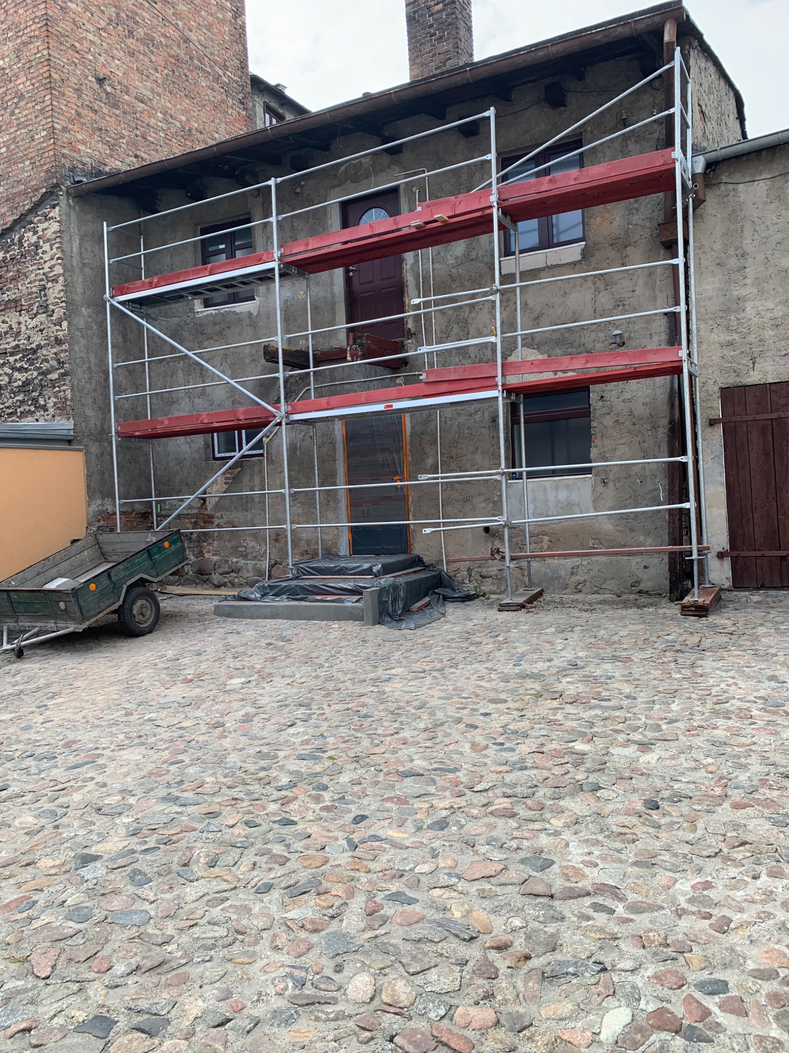 Rusztowanie ustawione przed kamienicą w Chełmnie, przygotowania do remontu elewacji, widoczny fragment przyczepki.